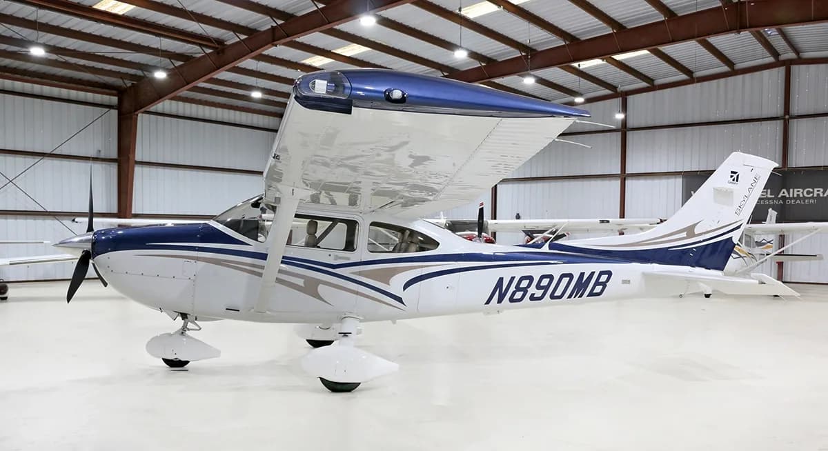 A white and blue Cessna Skylane N890MB is parked in a hangar, viewed from the side.