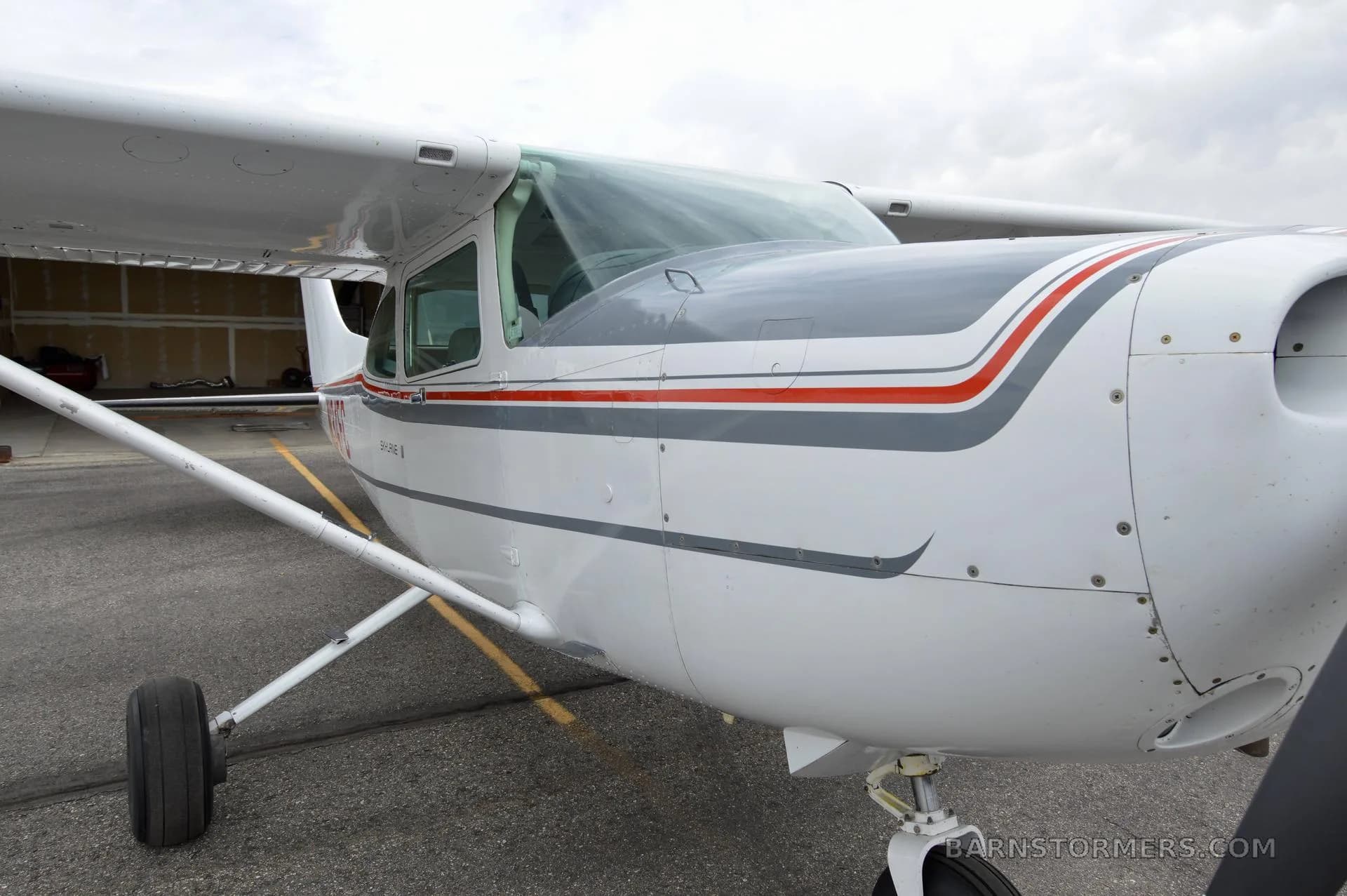 A close-up view of the front fuselage and wing of a white Cessna 182 Skylane with red and gray stripes.