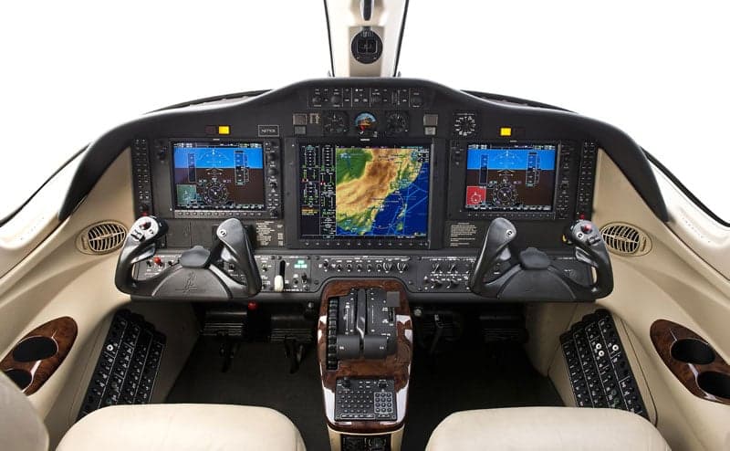 The cockpit of an aircraft features a modern glass panel display and cream-colored leather seats.