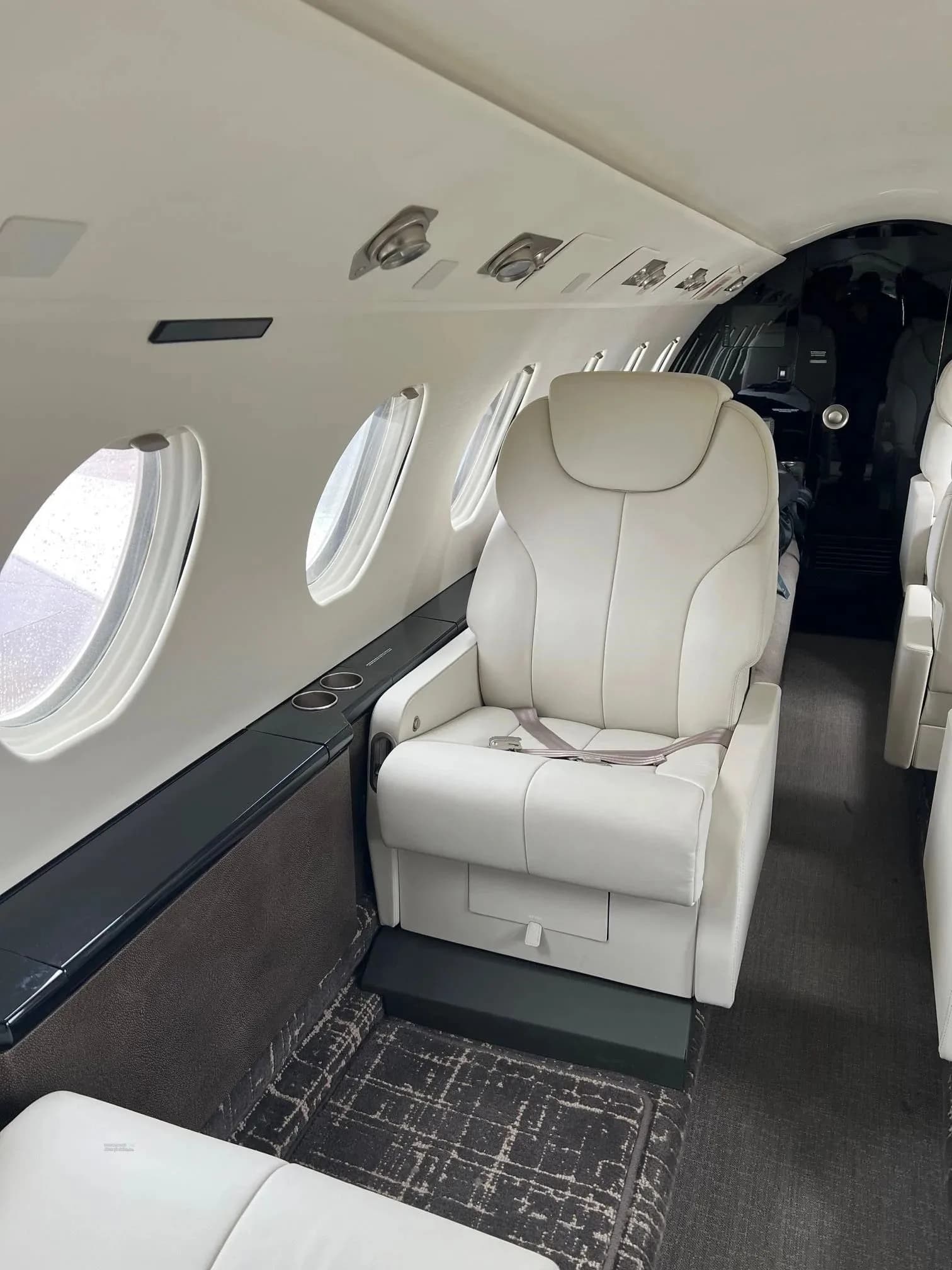 A view of the business jet cabin, showing white leather seats and windows along one side.