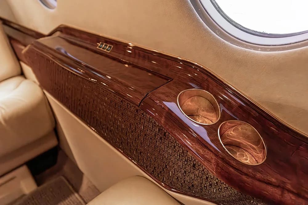 Close-up of a private jet's interior side panel with dark wood trim, cup holders, and a window.