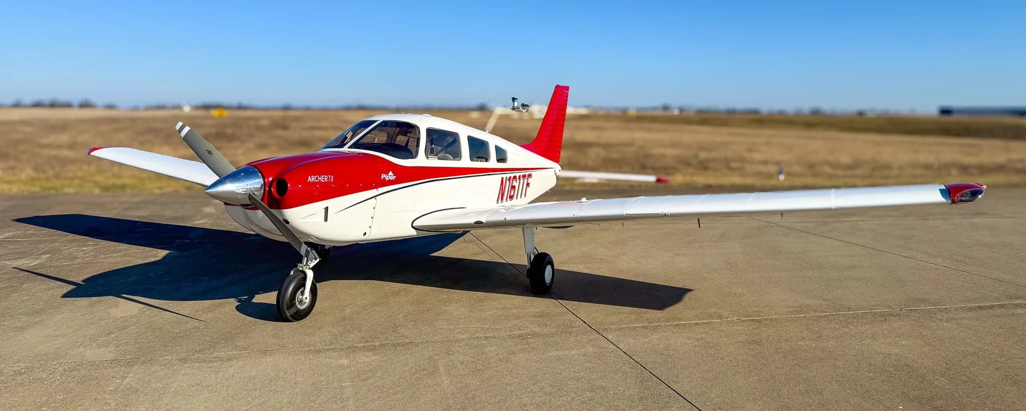 A red and white Piper Archer TX aircraft, tail number N161TF, parked on an asphalt tarmac under a clear blue sky.