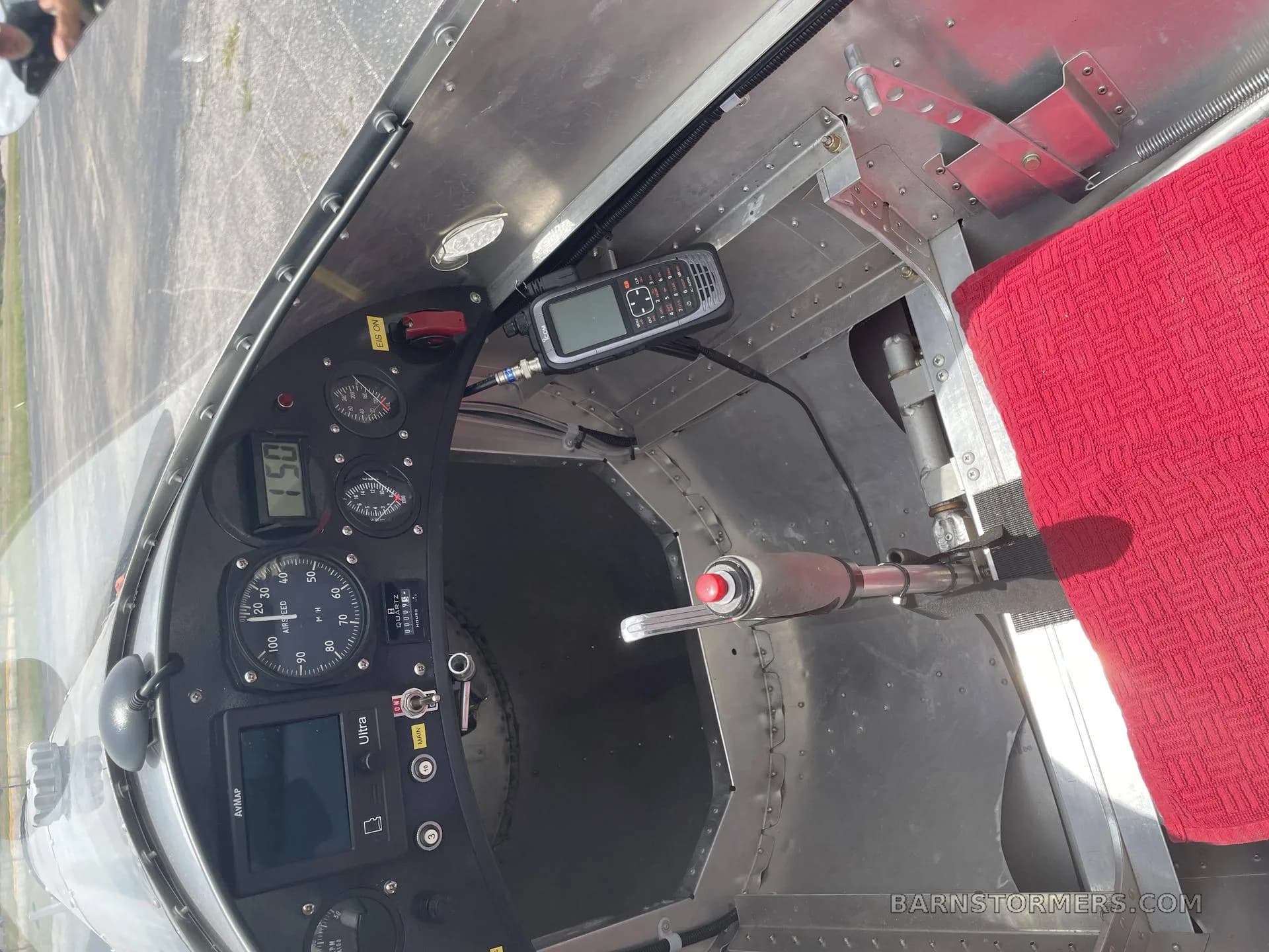 An overhead view of the aircraft's cockpit, showing the instrument panel, stick, and a red seat cushion.
