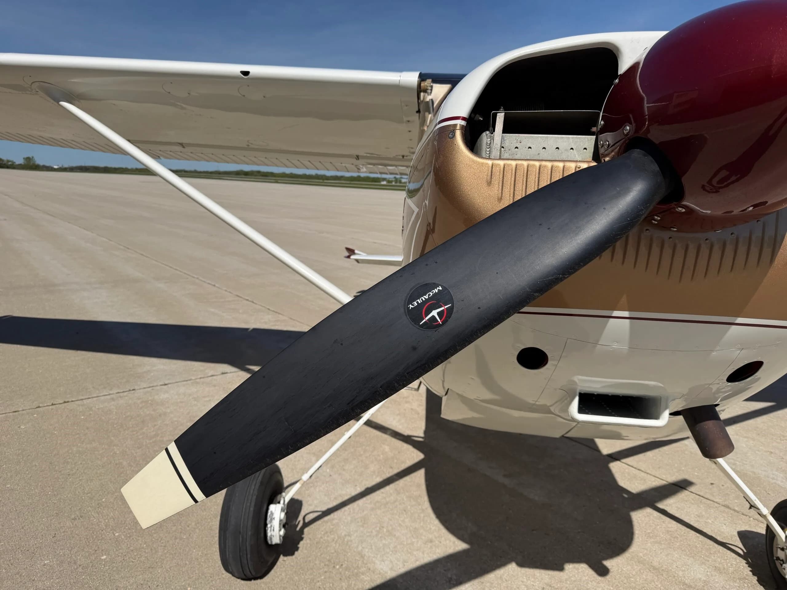 Close-up of the propeller and front cowling of a white, gold, and maroon Cessna 172.