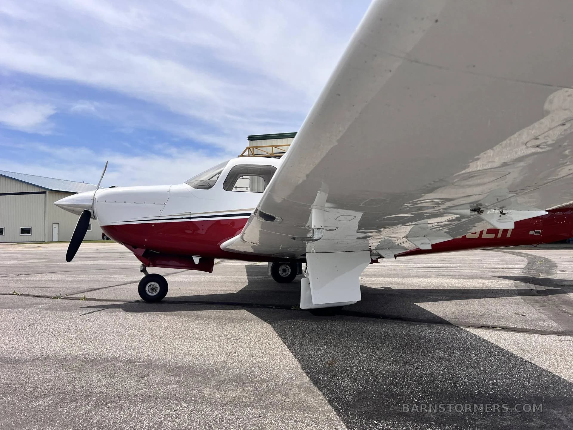 A side view of a white and red single-engine propeller aircraft, showing the underside of its wing.