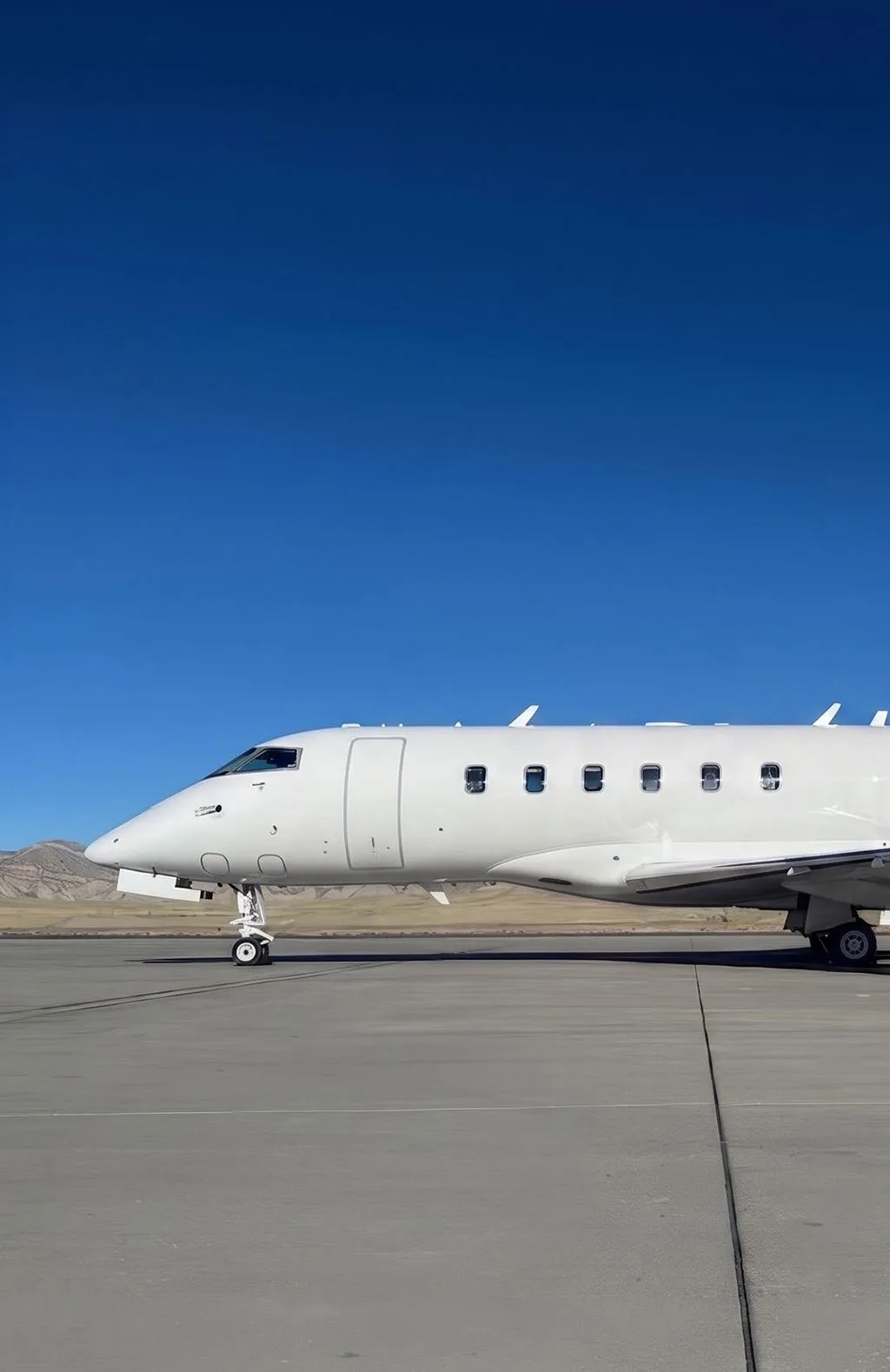 A close-up side view of the front fuselage of a white Bombardier Challenger 605 business jet on an airfield.