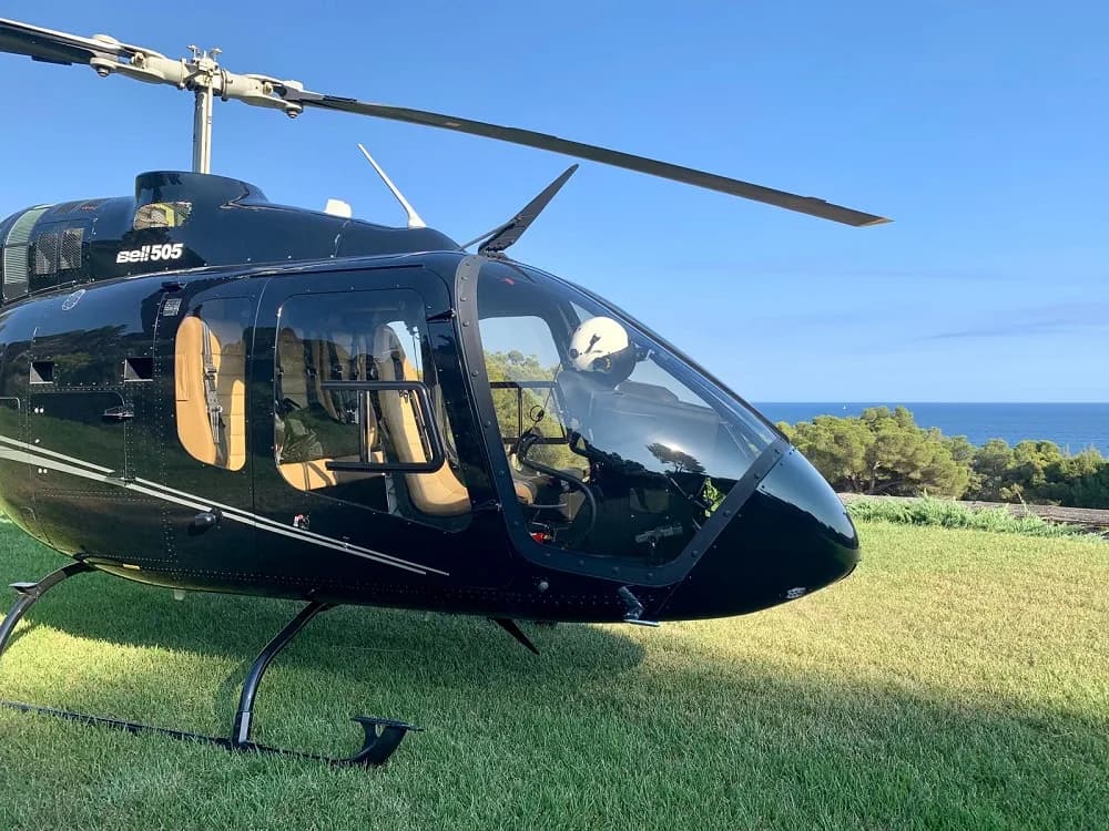 Bell 505 helicopter parked on the grass with a black paint scheme.