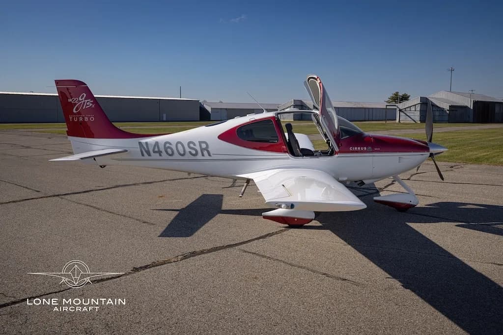 A side view of a white and maroon Cirrus SR22T aircraft with registration N460SR, parked on an airfield with its doors open.