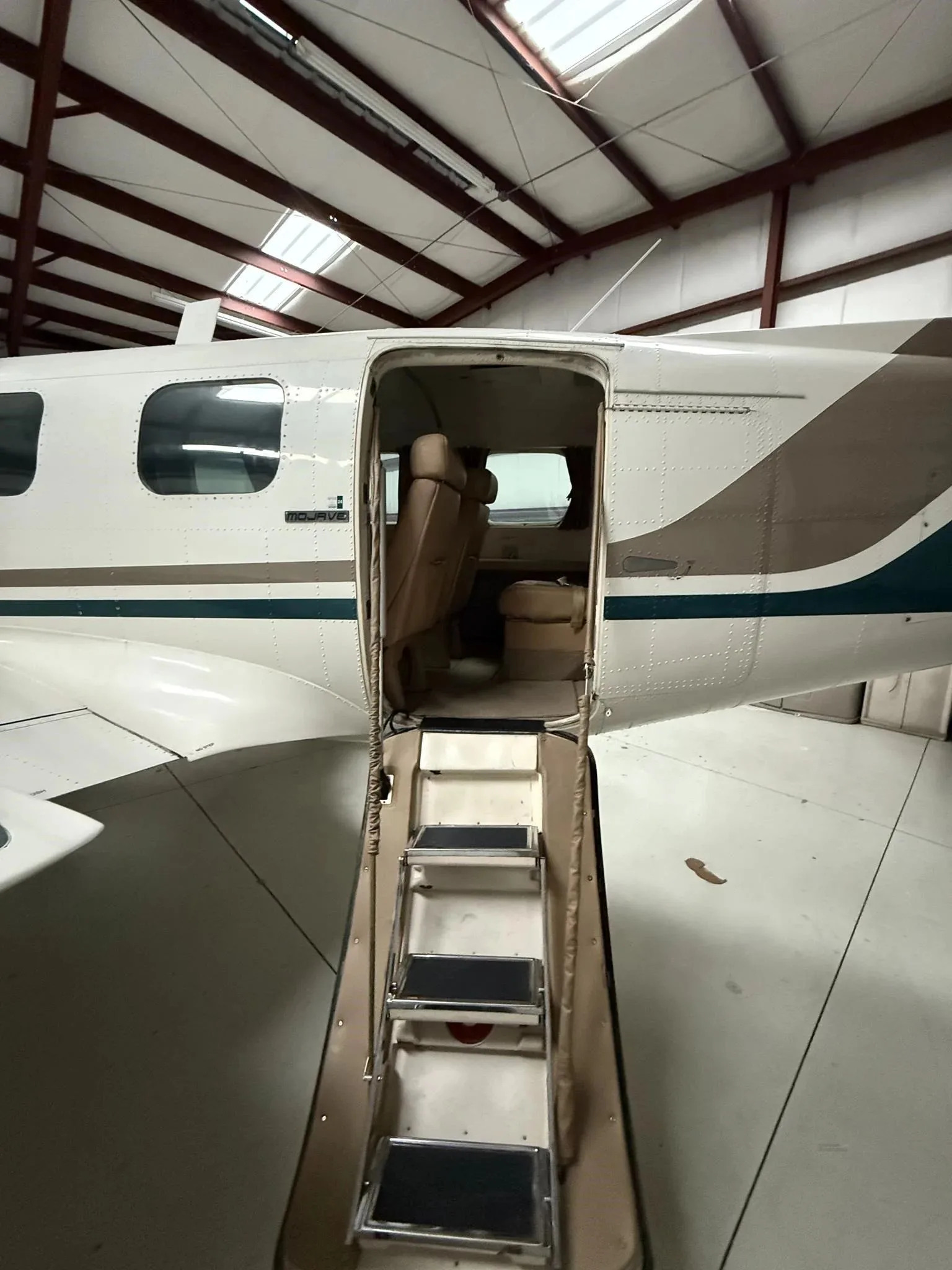 The open passenger door and retractable steps of a Piper Navajo aircraft, showing the tan interior.