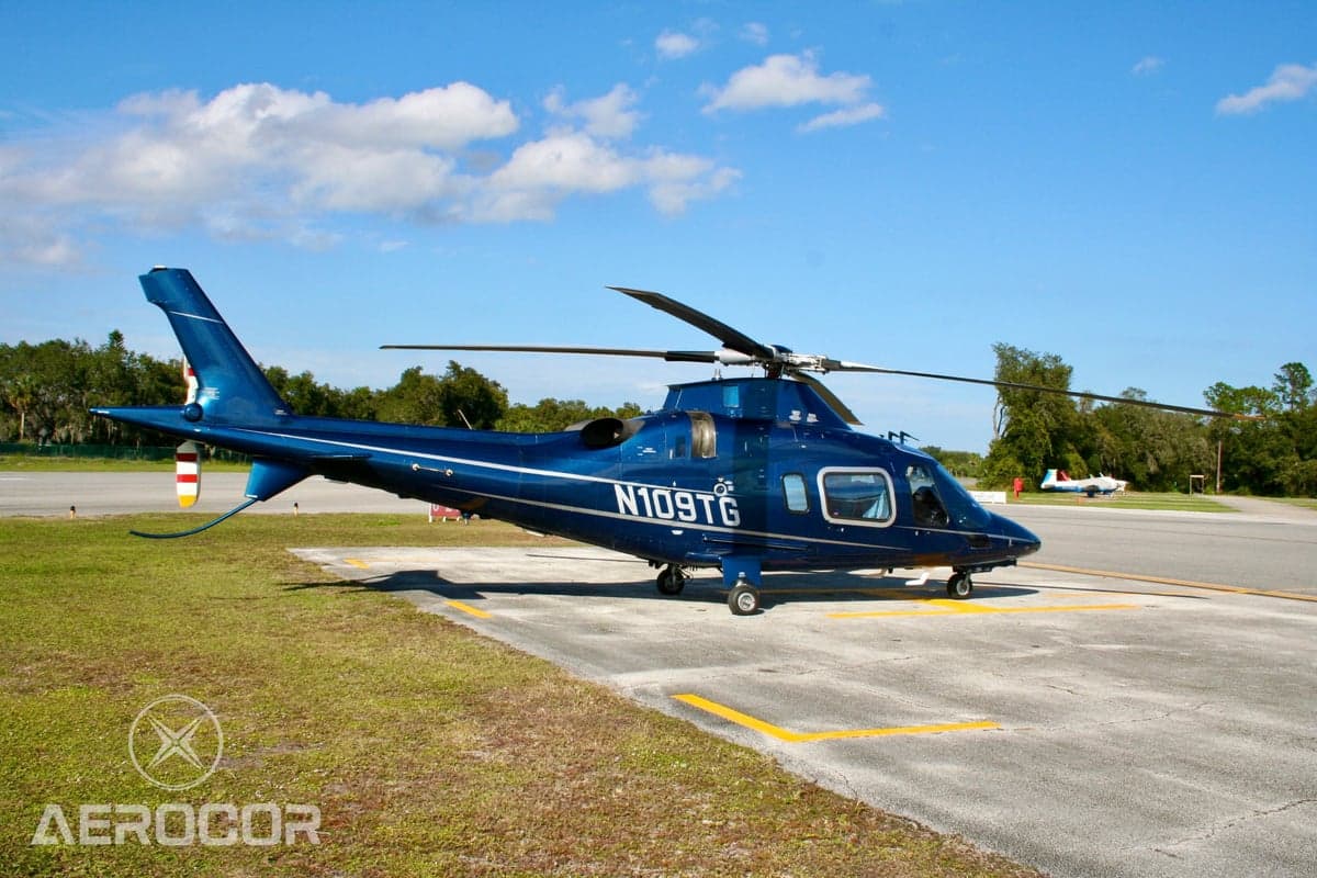 Three-quarter rear view of a blue AgustaWestland AW109 helicopter (N109TG) parked on an airfield.