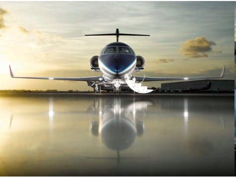 Front view of a private jet on a wet tarmac at sunset.