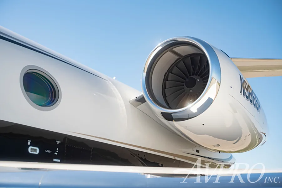 A close-up view of the polished engine and a round window on the white fuselage of the Gulfstream G550 (N986SP).