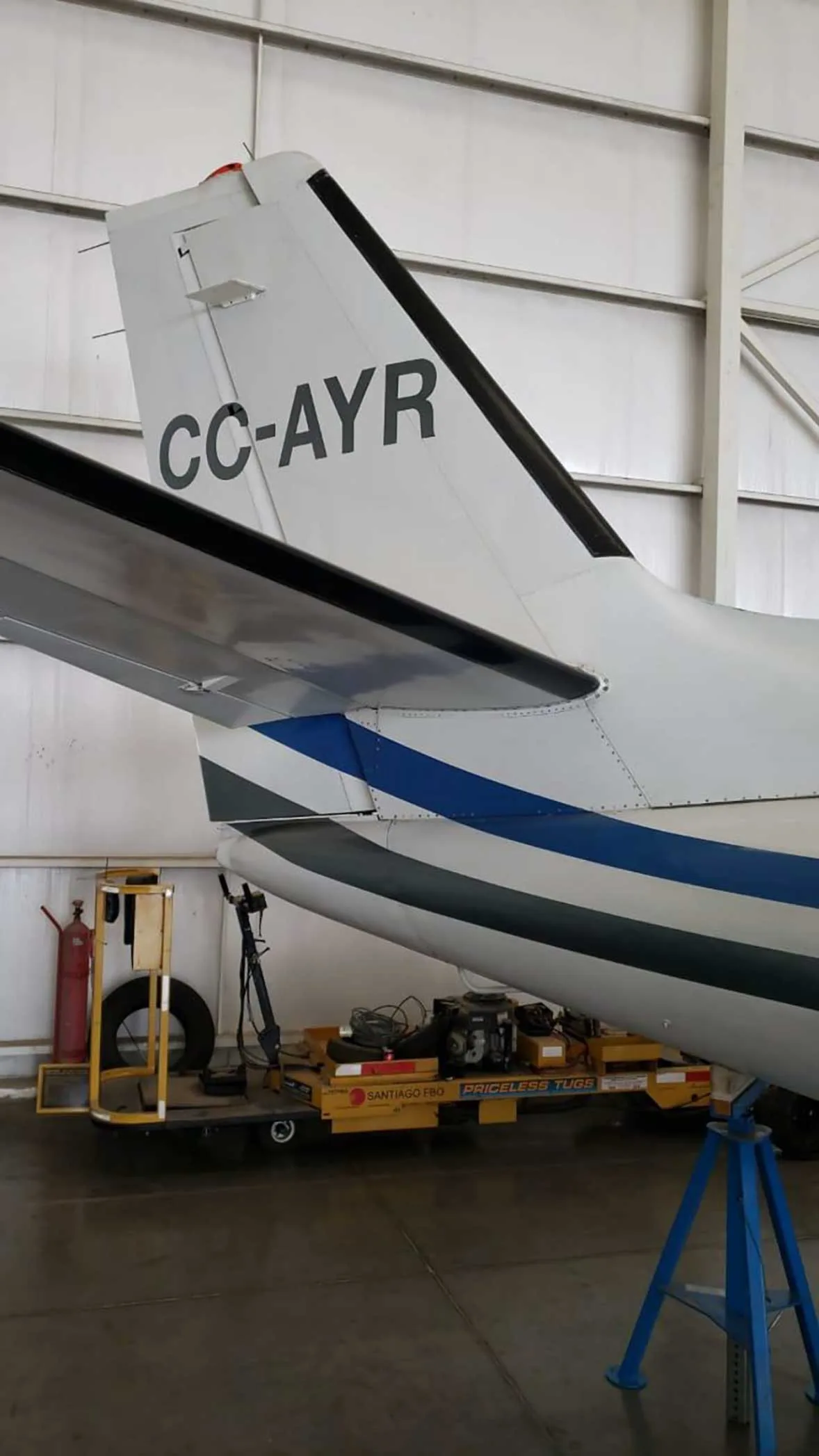 The tail section of a white business jet with blue and grey stripes and registration CC-AYR, inside a hangar.