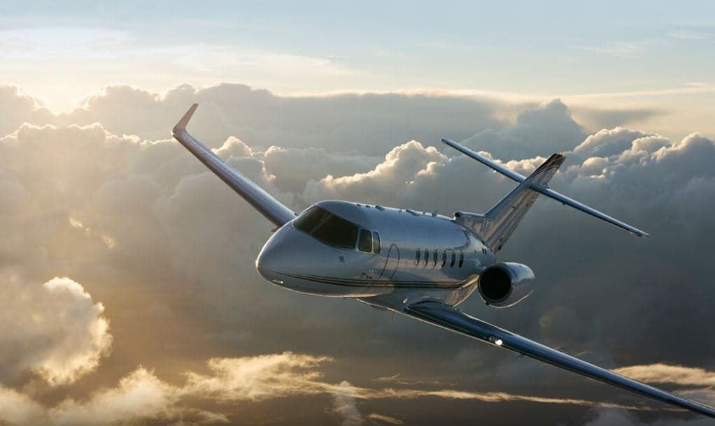 A Citation Latitude aircraft in flight against a cloudy sky.