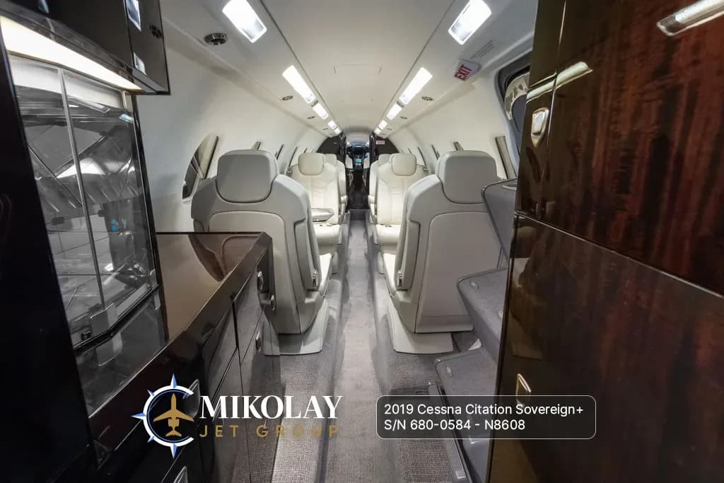 View of the aircraft cabin interior with light-colored leather seats and dark wood paneling, looking towards the front.