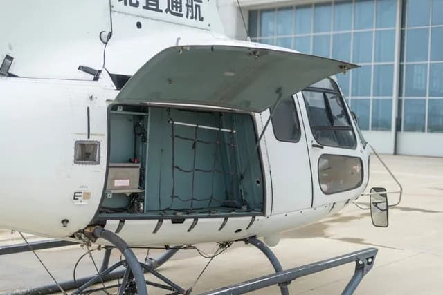 The front section of a white helicopter with its cargo door open, revealing a netted storage area.