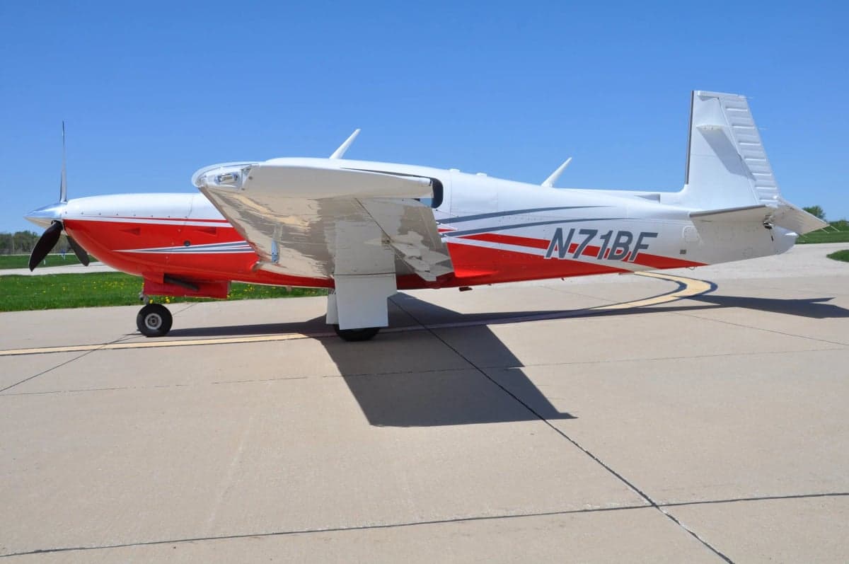 A Mooney M20J aircraft with a white and red paint scheme parked on the tarmac, showing the tail number.