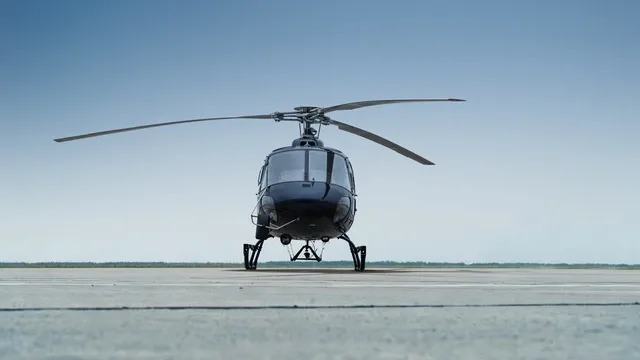 A dark blue helicopter, viewed from the front, parked on an airfield.