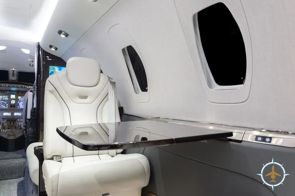 A close-up of a white leather cabin seat with a fold-out table extended.