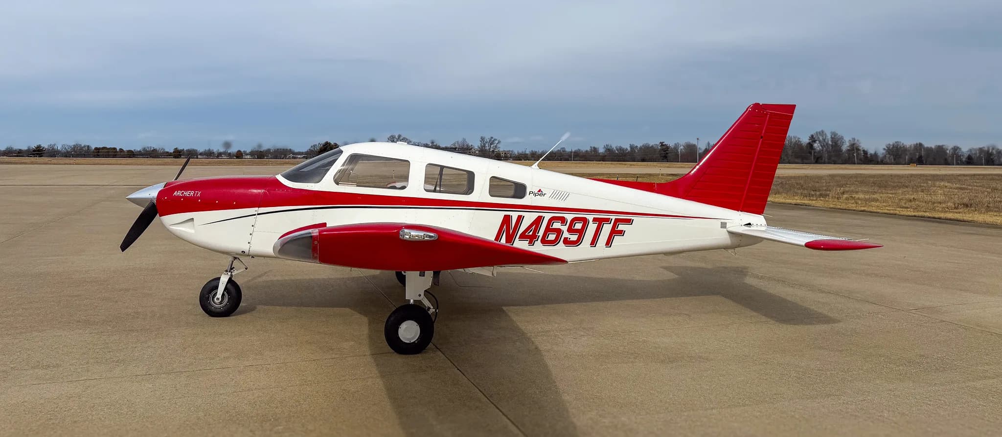 A side view of a white and red Piper Archer TX aircraft, N469TF, parked on an airfield.