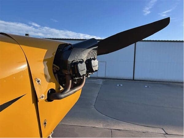 Close-up view of the exposed engine and propeller of a yellow Legend Cub aircraft on an airfield.