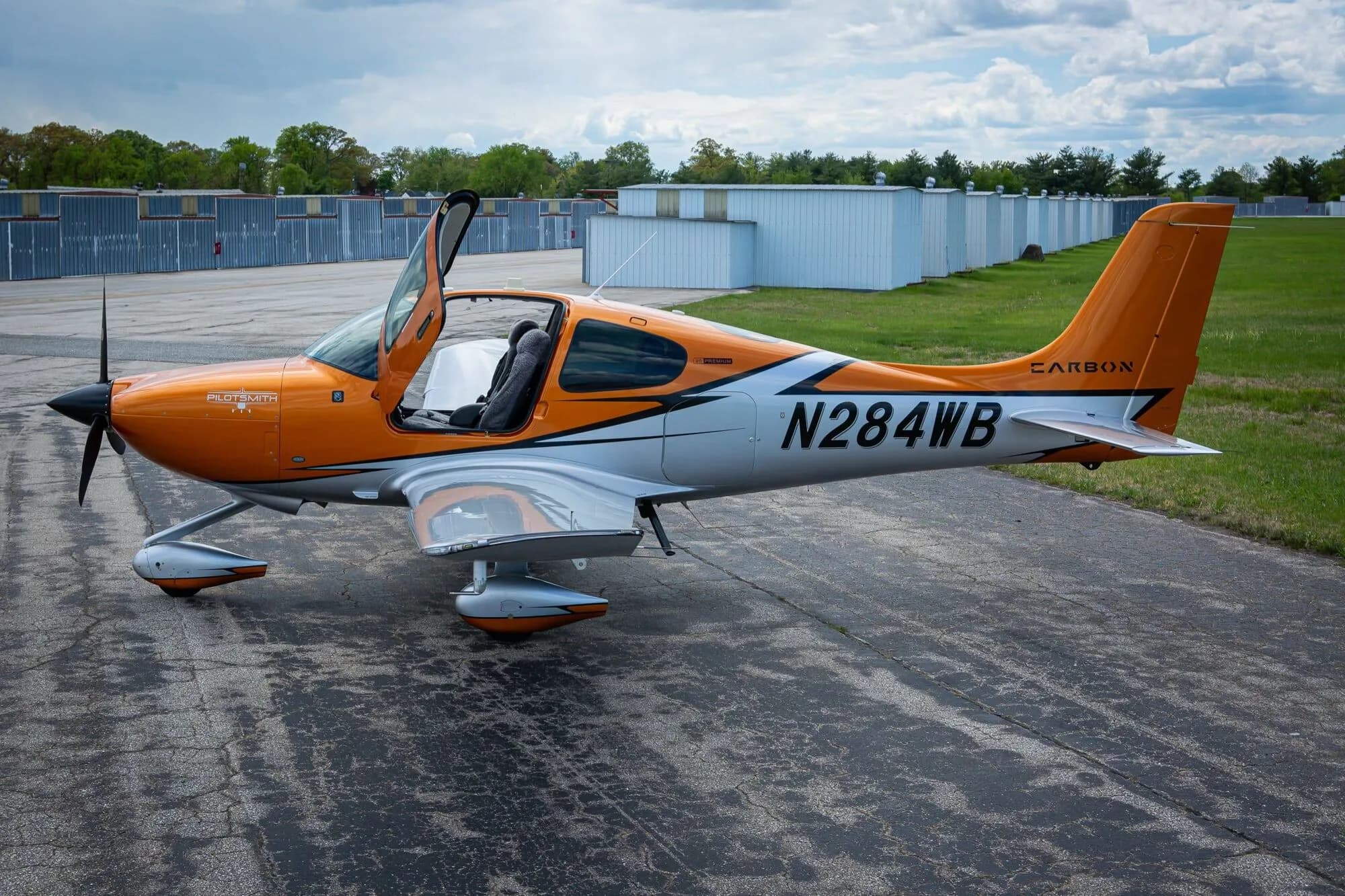 A side view of an orange and silver Cirrus SR20 aircraft, N284WB, with the pilot's door open on an airfield.