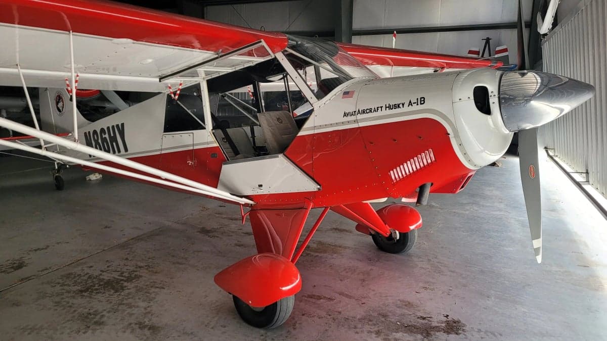 Aviat Aircraft Husky A-1B aircraft with a red and white paint scheme inside a hangar.