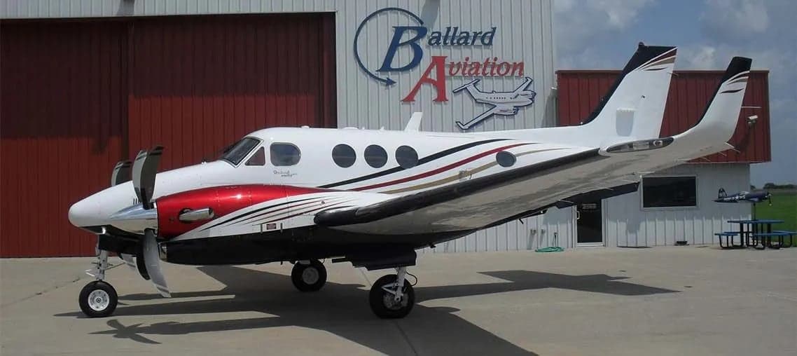 A Beechcraft King Air sits on the tarmac in front of a hangar.