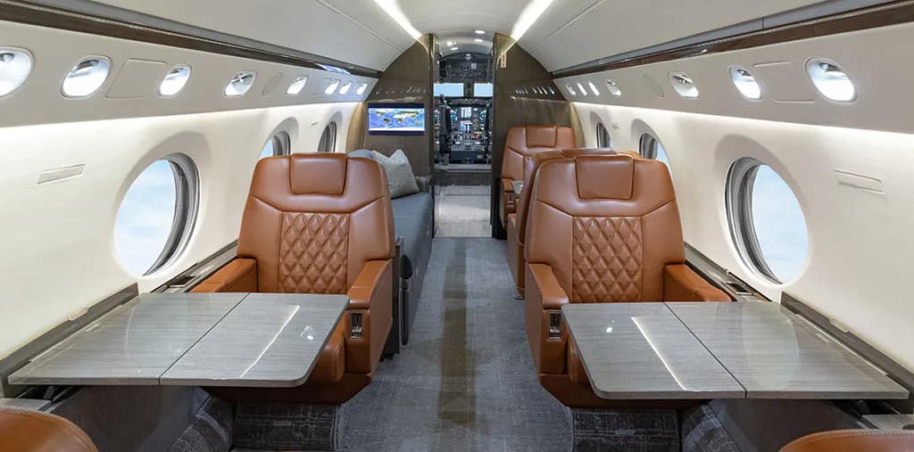 A wide view of the aircraft cabin interior, showing two sets of brown leather seats with tables.