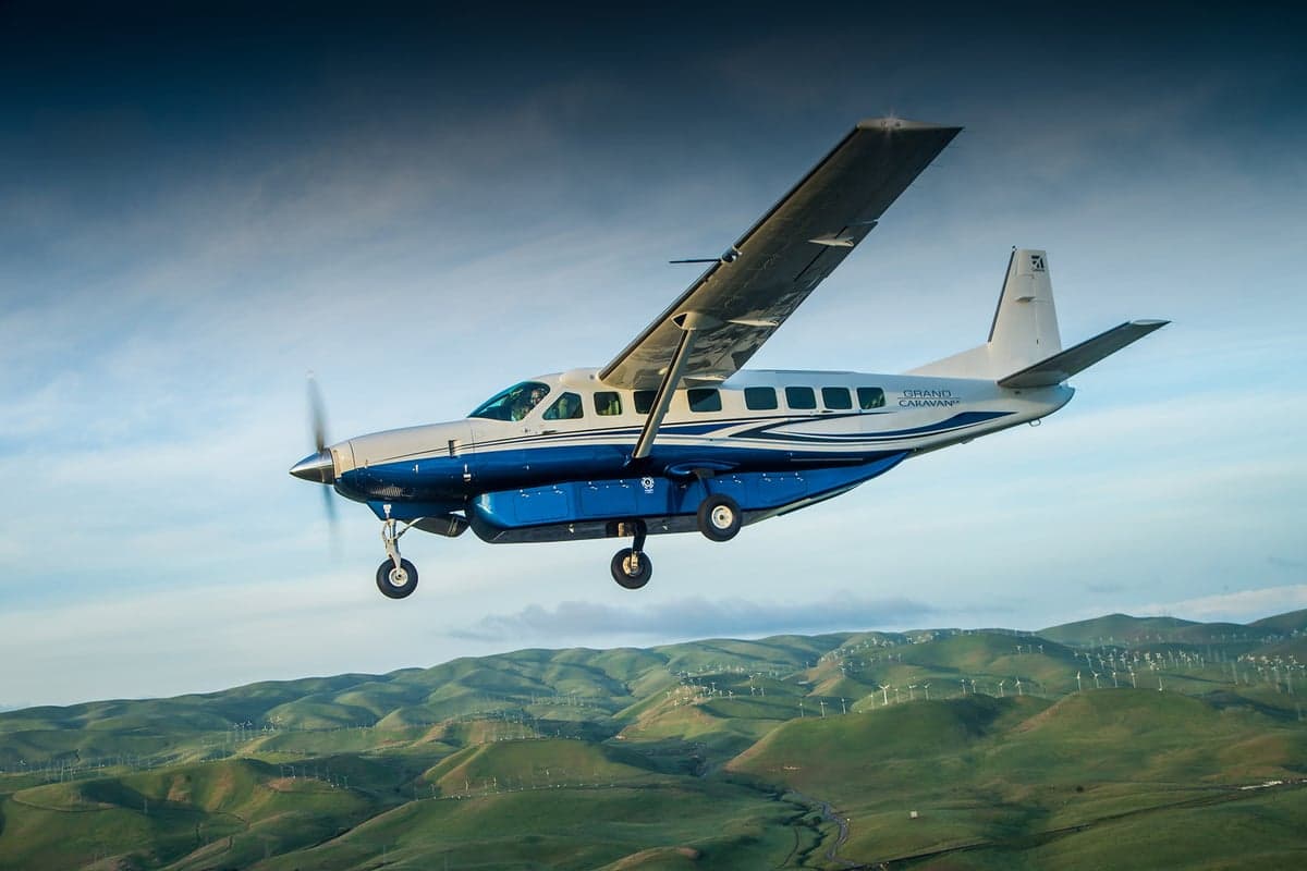 A Cessna Grand Caravan in flight over a hilly landscape.