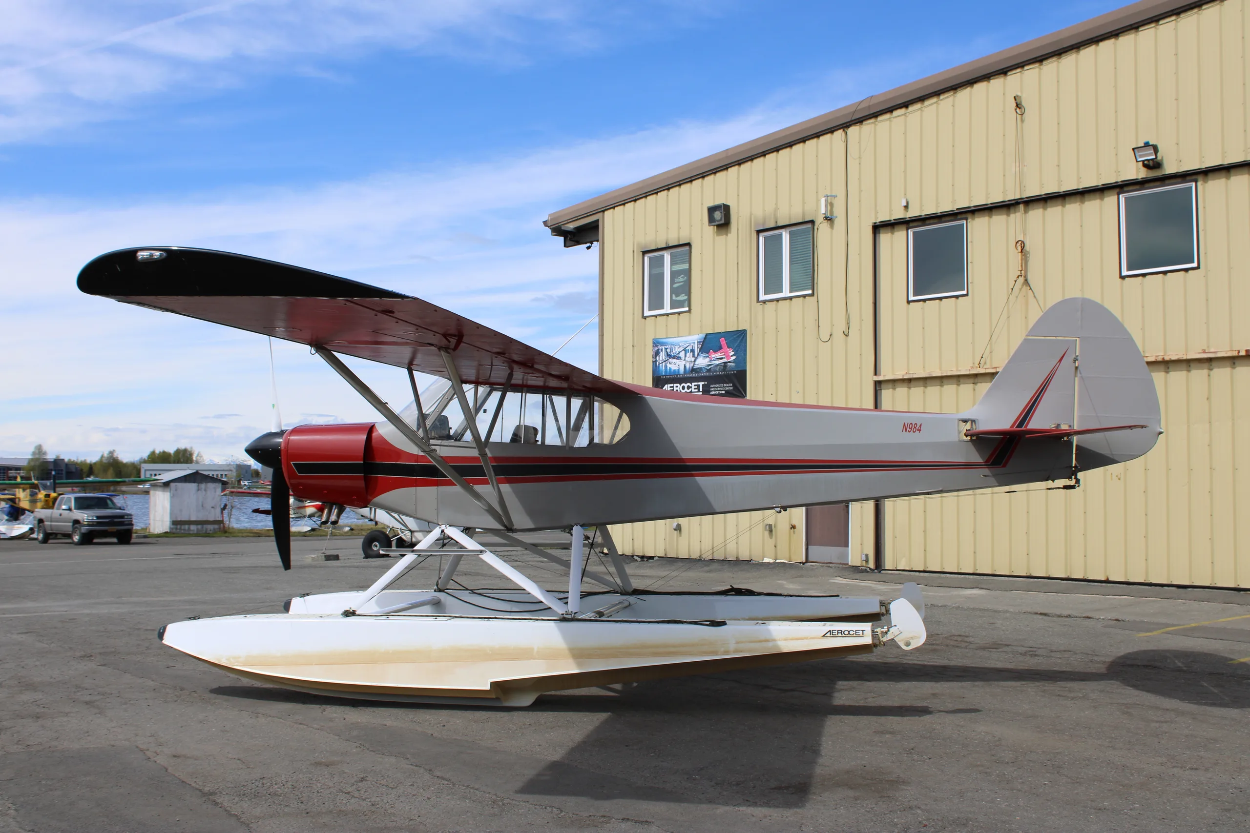 A red and silver float plane is parked on the tarmac, side view.