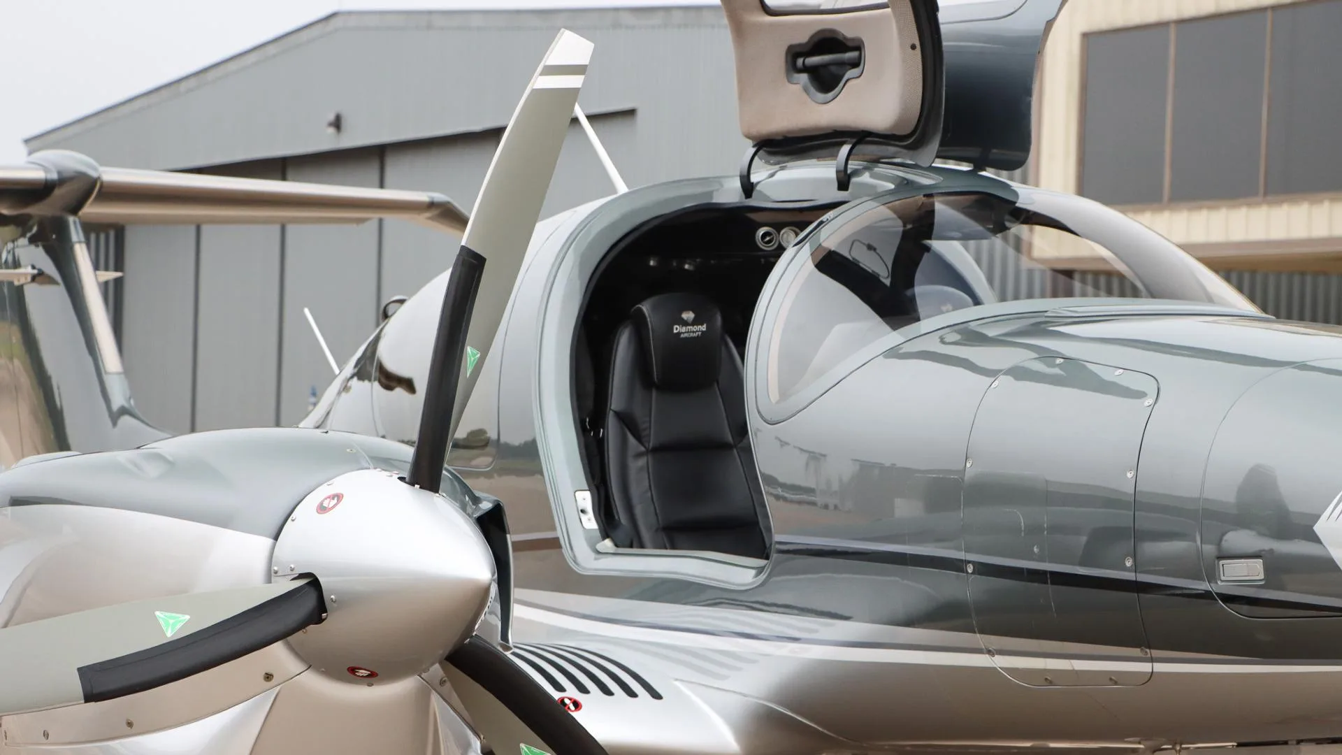 A close-up of the open gull-wing door of the Diamond DA62 aircraft, showing a black leather seat with the Diamond Aircraft logo.