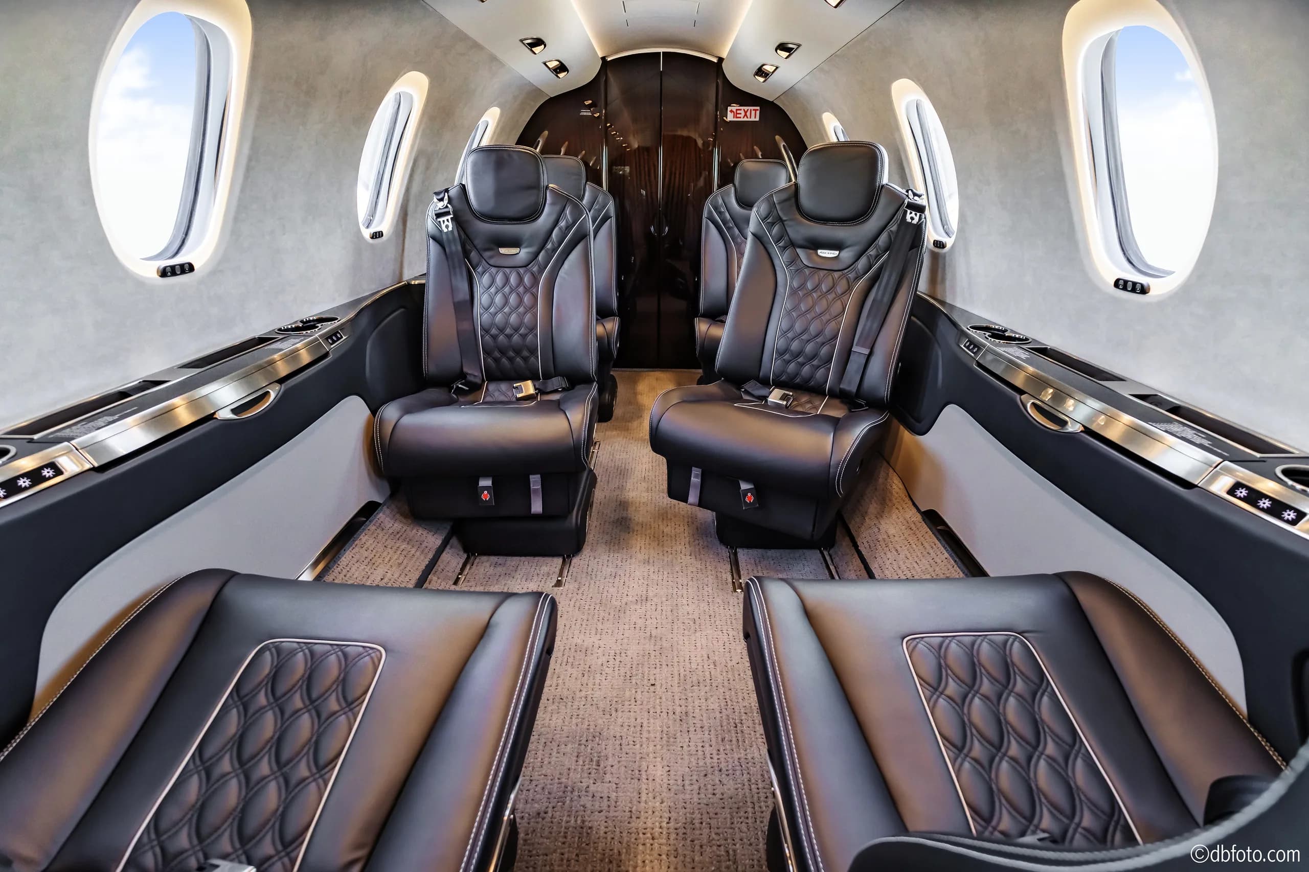 The luxurious interior cabin of the business jet features black quilted leather seats and light gray walls.