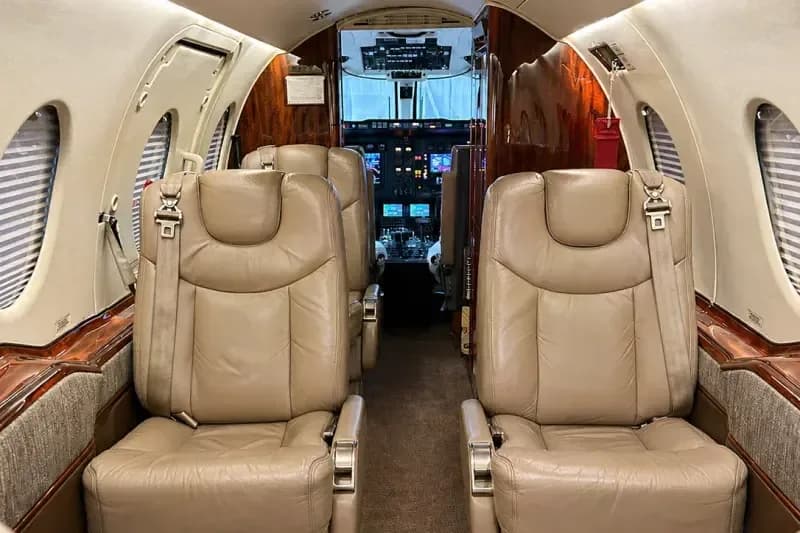 The aircraft's interior cabin features beige leather seats and wood paneling, looking towards the cockpit.
