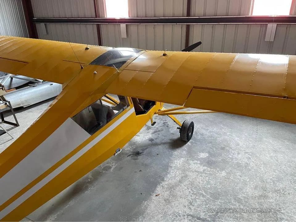 Top-down view of the yellow high-wing aircraft's wing and fuselage inside a hangar.