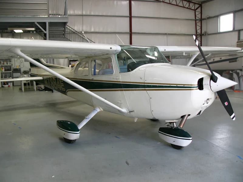 A white single-engine propeller aircraft with dark green and gold stripes, tail number N7384E, parked inside a hangar.