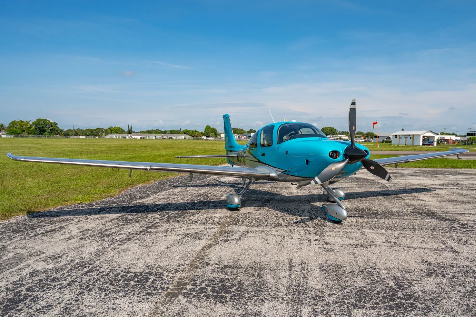 A front three-quarter view of a blue and silver Carbon aircraft (N33JG) parked on an asphalt ramp with a red flag in the distance.
