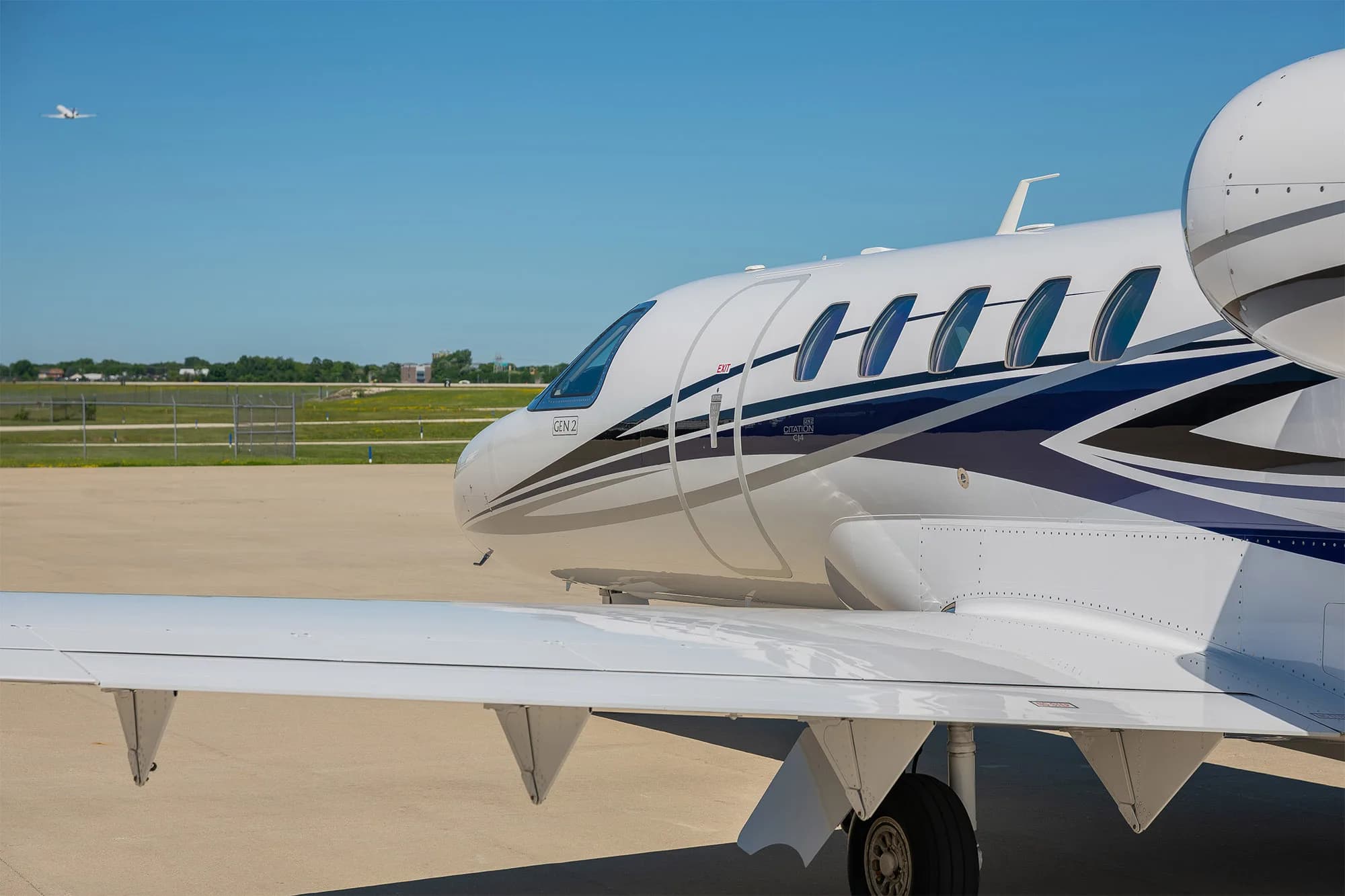 A close-up view of the front fuselage and wing of a white Cessna Citation Latitude jet with blue and grey stripes, tail number N417NE, on a tarmac.