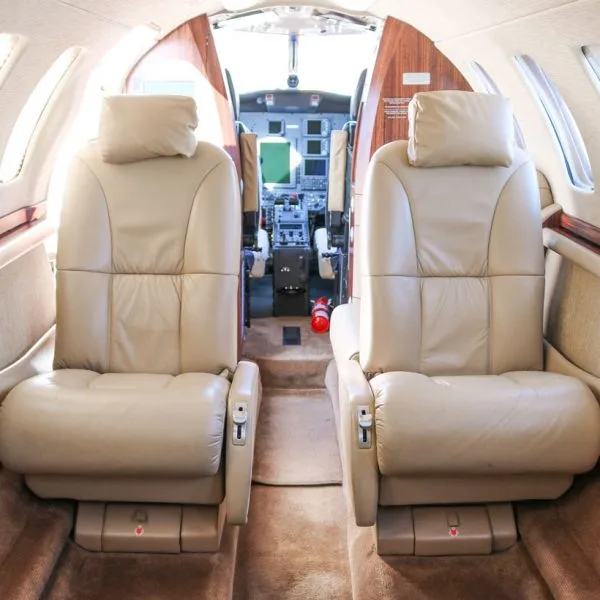 Interior view of an aircraft cabin with beige leather seats, looking towards the cockpit.
