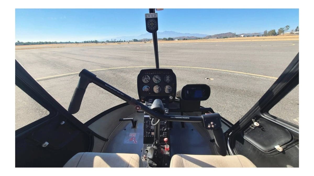 A wide view of the Robinson R22 helicopter cockpit, showing the instrument panel, cyclic, and collective controls.