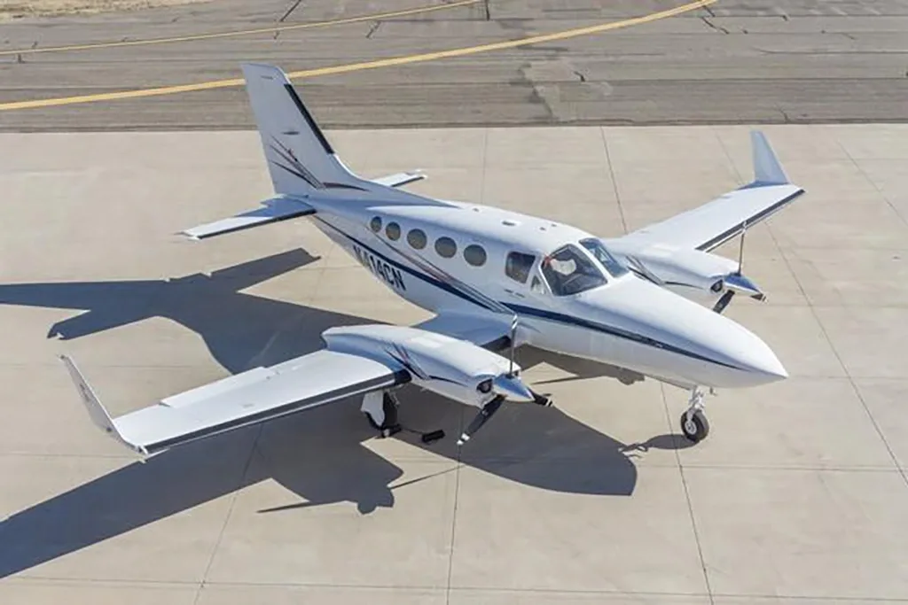 An overhead view of the white Cessna 414 Chancellor N414CN with blue and black stripes on an airfield.