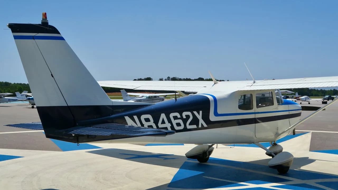 A rear-right view of a white Cessna 172 with blue and black stripes, N8462X, parked on an airfield.