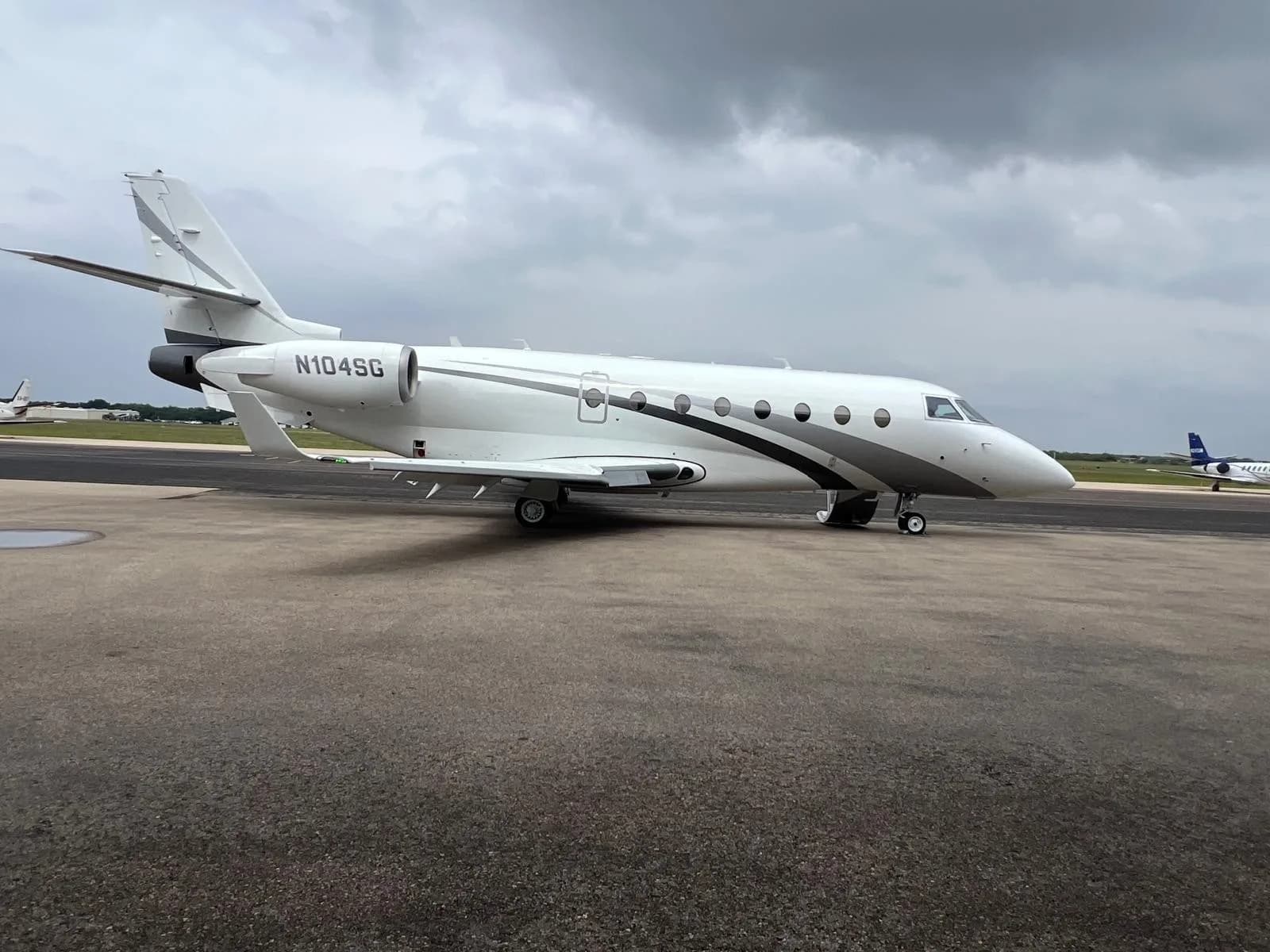 A white and gray jet with tail number N104SG sits on the tarmac under a cloudy sky.