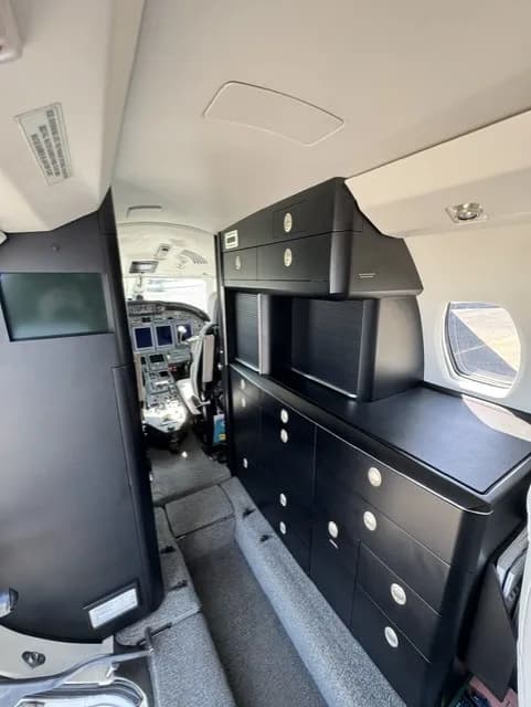 The interior of a business jet, showing dark cabinetry and a view towards the cockpit.