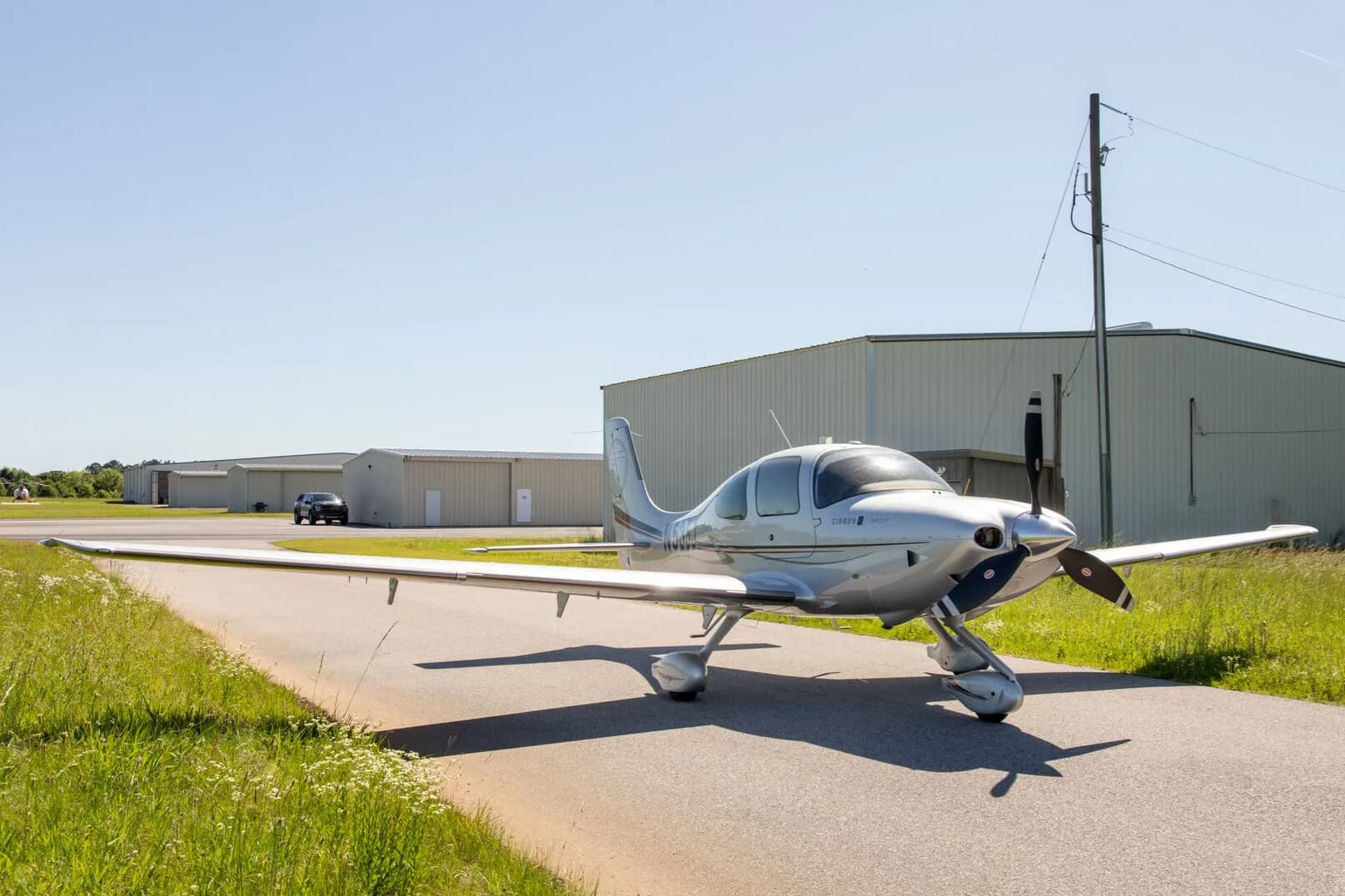 A silver Cirrus SR22T aircraft with registration N535J is parked on an asphalt strip with hangars and a car in the background.