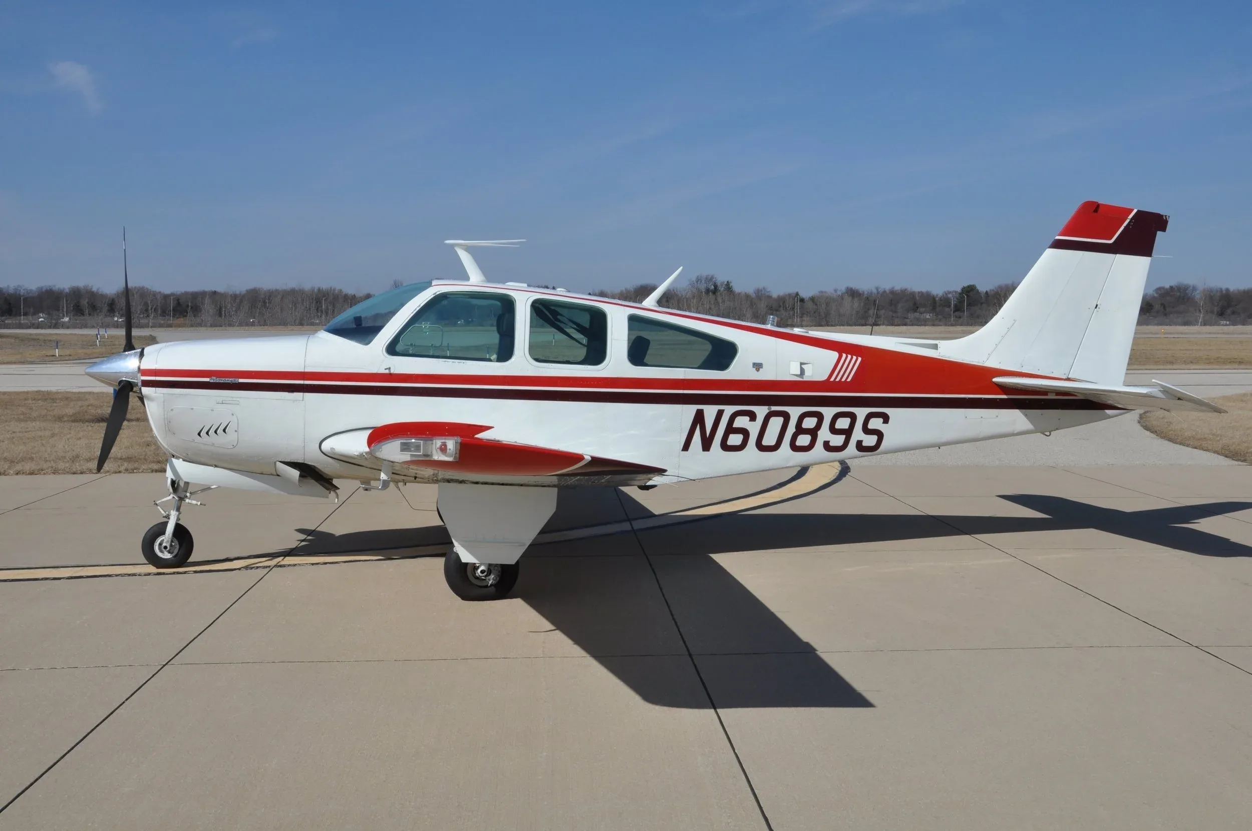 A white single-engine propeller aircraft with red and brown stripes and registration N6089S parked on an airfield.