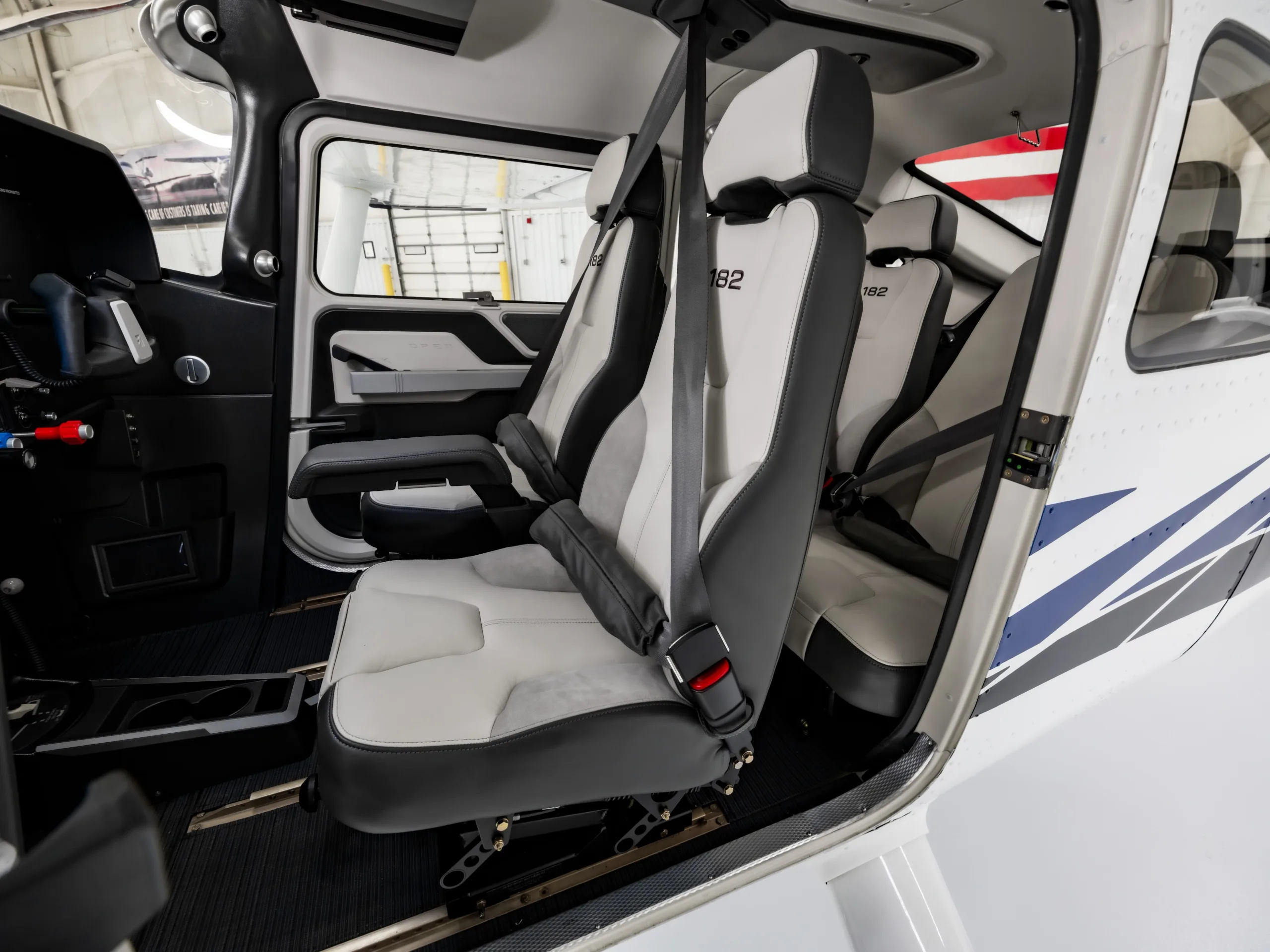 The light gray and dark gray interior seats of a Cessna 182 aircraft cabin are visible from the side.