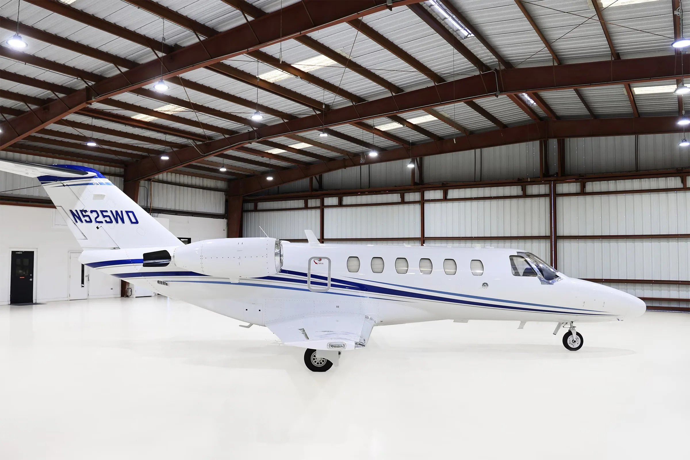 A white Cessna Citation CJ2+ (N525WD) with blue stripes parked in a hangar, viewed from the right side.