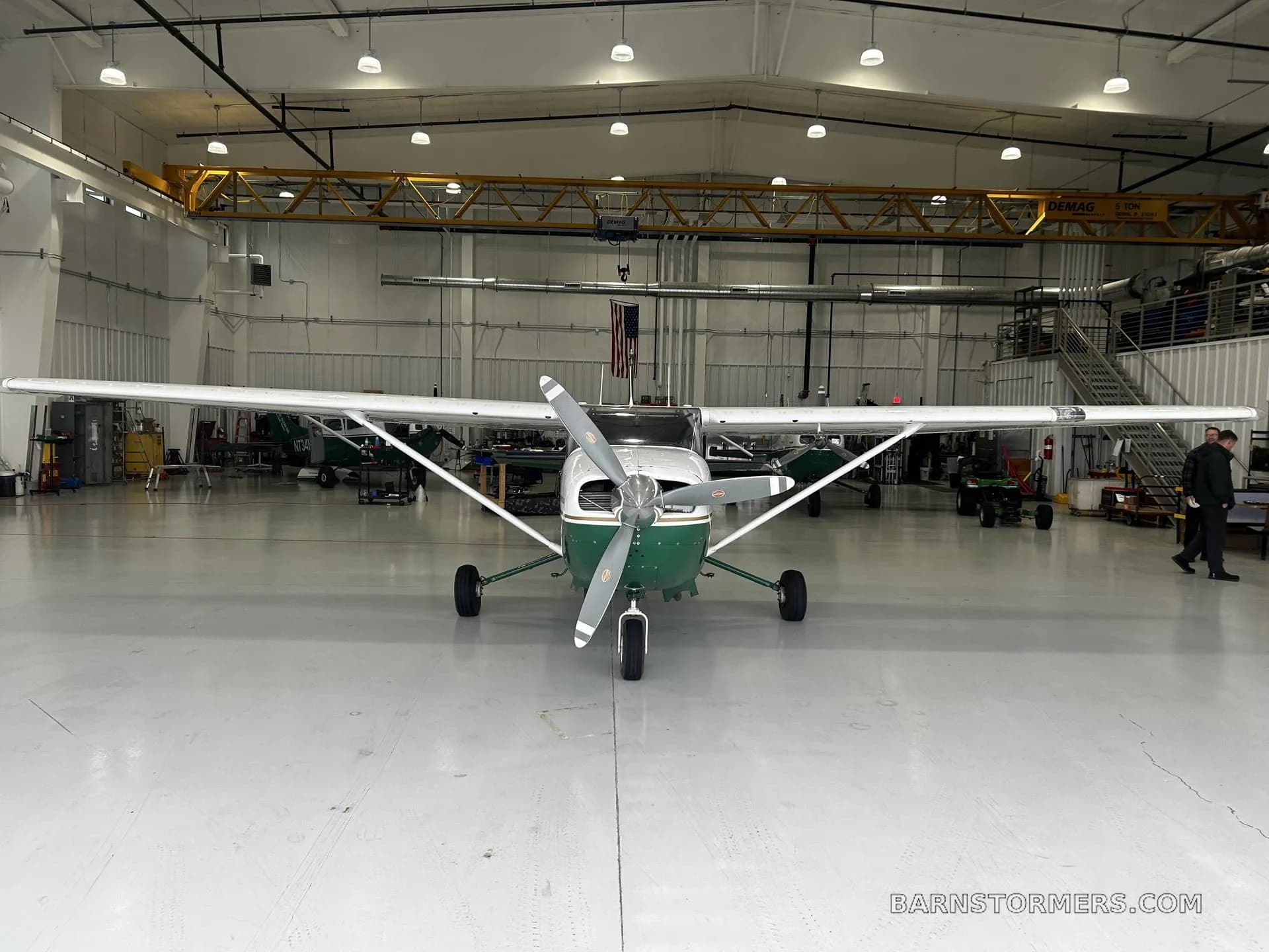 A white and green Cessna 207 Stationair aircraft is parked head-on in a brightly lit hangar.