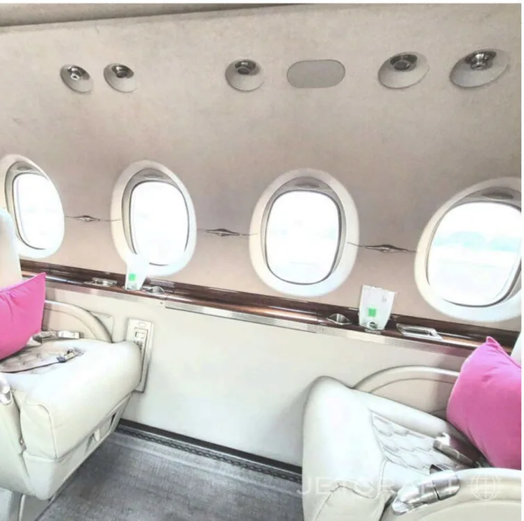 A view of the aircraft cabin with four oval windows above cream-colored seats and pink pillows.